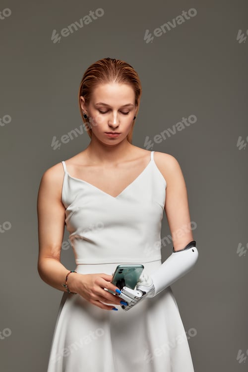 Preview: Studio portrait of young girl in white dress wearing sensory bionic prosthetic arm. Charming blonde