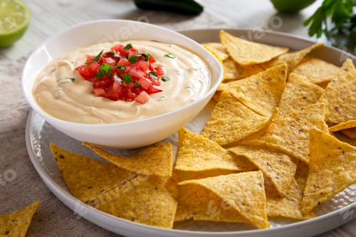 Preview: Homemade cheesy dip in a bowl, yellow tortilla chips, side view. Close up.