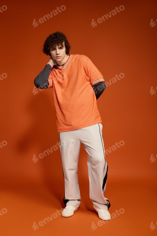 Preview: Curly-haired teenager dressed in casual style against a vibrant orange background