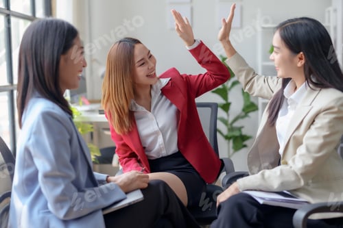 Preview: Asian female business colleagues giving high-five in a team meeting at office.