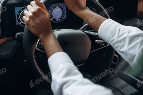 Preview: Two hands are on the steering wheel. Woman in white shirt is in the modern car