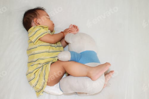 Preview: Toddler baby child girl sleeping with a teddy bear on the bed.