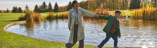 Preview: family bonding, happy african american woman following son, walking along pond, hold hands, banner