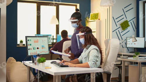 Preview: Businesswoman with protective mask discussing with african colleague