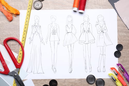 Preview: Sketch of stylish clothes and other fashion designer`s supplies on wooden table, flat lay