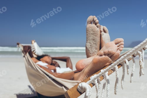 Preview: Front view of romantic young multi-ethnic couple relaxing on hammock at beach on sunny day