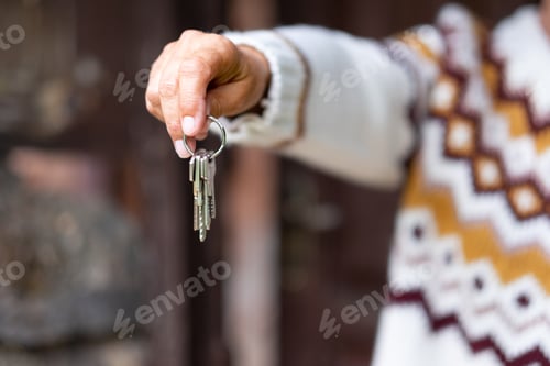 Preview: Caucasian hand of woman in winter sweater holding house keys in front to the wooden door.