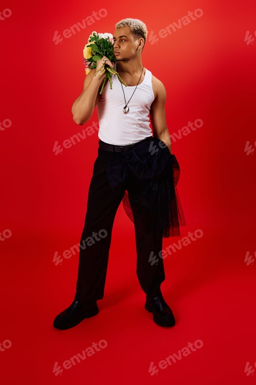 Preview: Stylish young African American man poses boldly with flowers in vibrant red studio