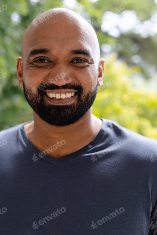 Preview: Portrait of smiling bald biracial man with beard standing on sunny balcony in front of treetops