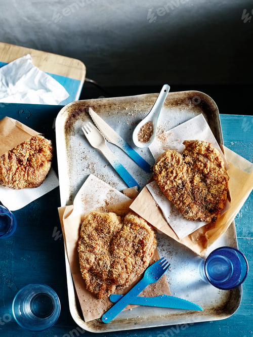 Preview: Breaded chicken cutlets served on a baking sheet with utensils