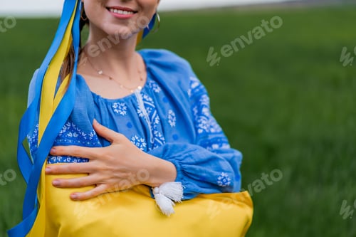 Preview: Smiling ukrainian woman with national flag on green field background. Young lady in blue embroidery