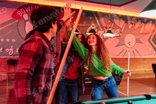 Preview: Friends giving high five while playing billiards in bowling alley