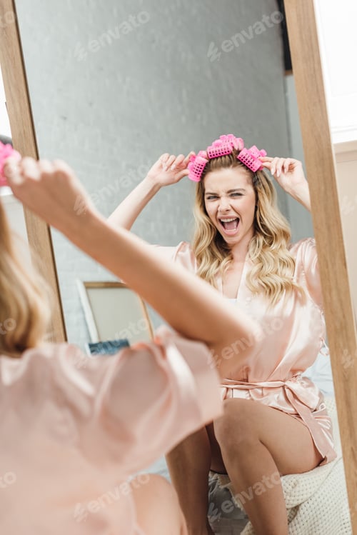 Preview: selective focus of excited girl touching pink hair curlers and looking at mirror