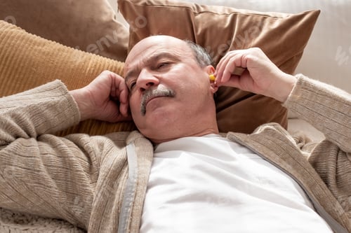 Preview: Senior stressed man holding a yellow earplug trying to sleep having insomnia
