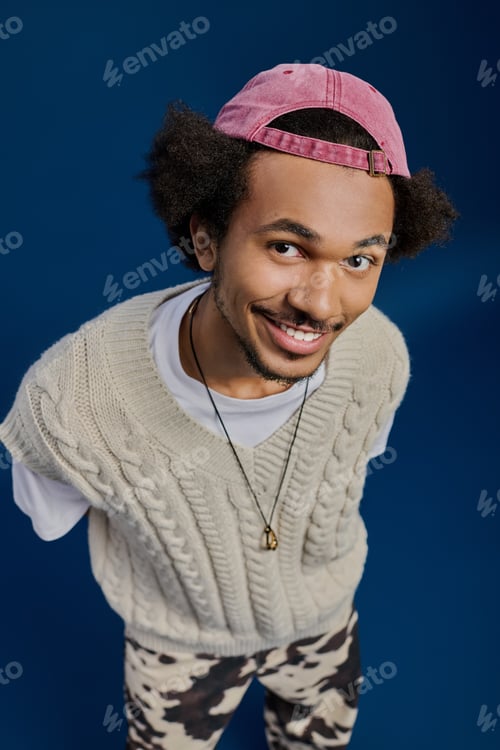 Preview: Charming young man poses playfully with a warm smile against a vibrant blue backdrop