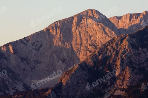Preview: Sunlit mountain peaks in a warm golden hue at sunset,