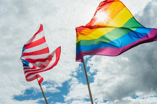 Preview: low angle view of american and colorful lgbt flags against blue sky with clouds