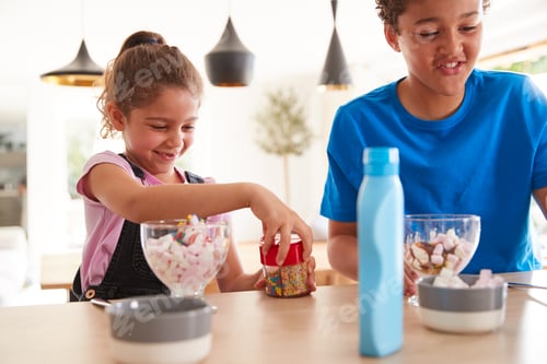 Preview: Children In Kitchen At Home Adding Sprinkles And Sauce To Ice Cream Dessert