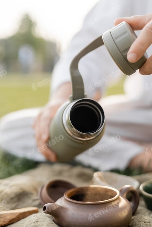 Preview: partial view of blurred man holding thermos near clay teapot during tea ceremony outdoors