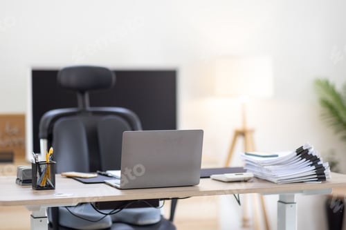 Preview: Laptop Computer, notebook, and eyeglasses sitting on a desk in a large open plan office space after