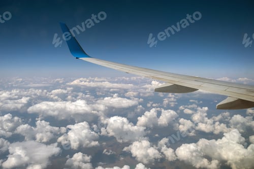 Preview: View of jet airplane wing from inside flying over white puffy clouds in blue sky.