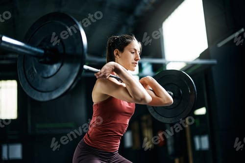 Preview: Female athlete exercising with barbell during strength training in a gym.