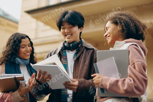 Preview: Group of happy young students standing outside college building with books and notepads