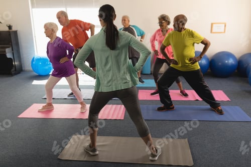 Preview: Rear view of young female trainer assisting a groupe of senior people in fitness studio
