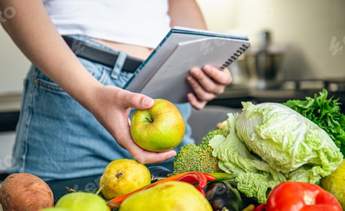 Preview: Woman with notepad and vegetables on the kitchen table preparing a recipe.