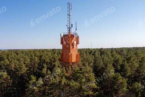 Preview: Communication tower stands tall among dense forest under clear blue sky