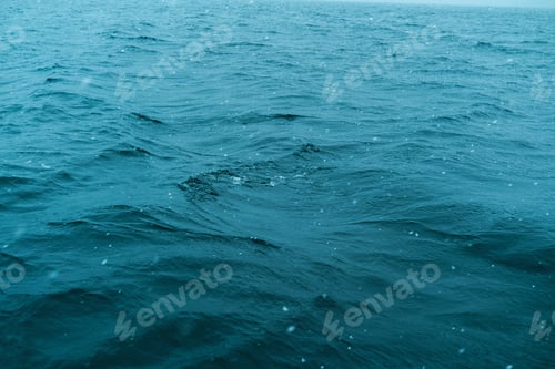 Preview: Deep blue ocean water surface with gentle waves and falling snow during overcast weather