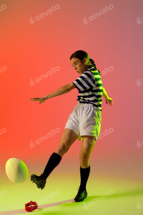 Preview: Caucasian female rugby player kicking rugby ball over neon pink lighting