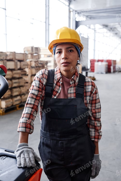 Preview: Young serious female engineer in workwear standing by cart with package