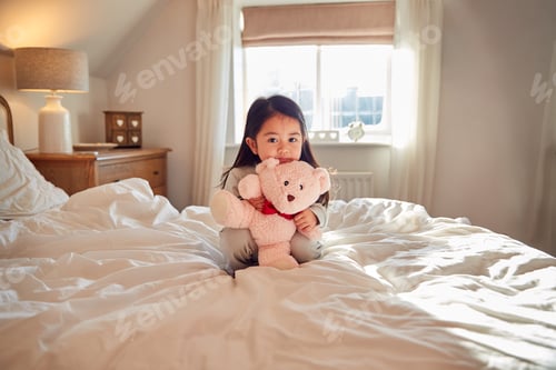 Preview: Young Girl Sitting On Bed Wearing Pyjamas At Home Cuddling Soft Toy