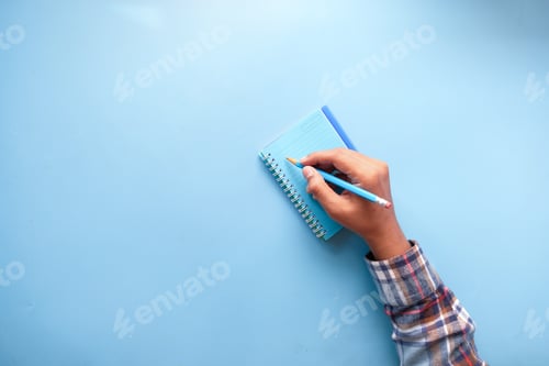 Preview: top view of man hand writing on notepad on blue background