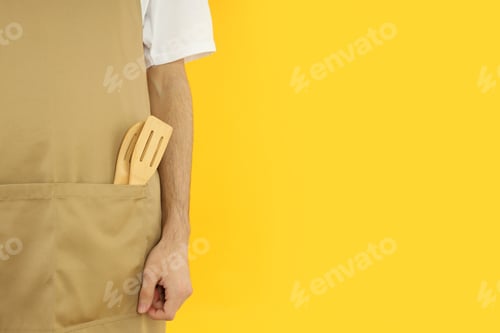 Preview: Young man in apron on yellow background, space for text