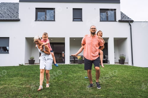 Preview: Young family standing outside their house each of the kids piggyback riding one of the parents