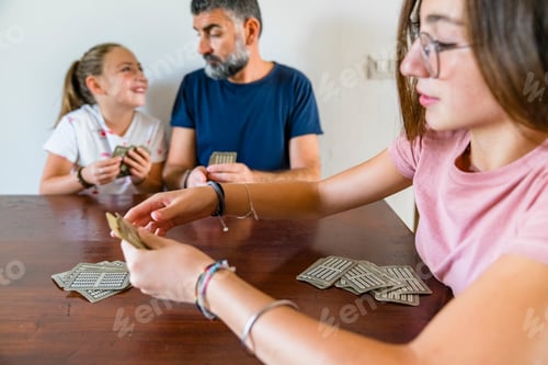Preview: Father with two daughters playing cards on wooden table at home