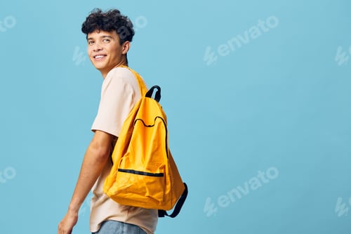 Preview: Young man with a yellow backpack on a blue background, smiling and looking back Ideal for lifestyle