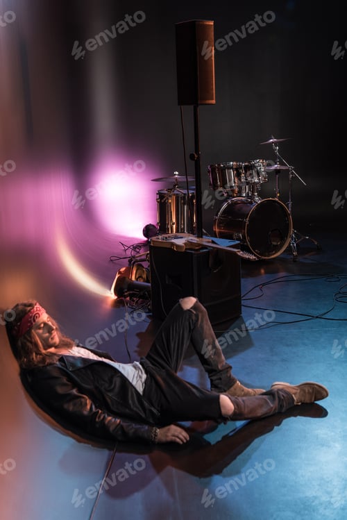 Preview: Young tired rock star sitting on floor near drums set