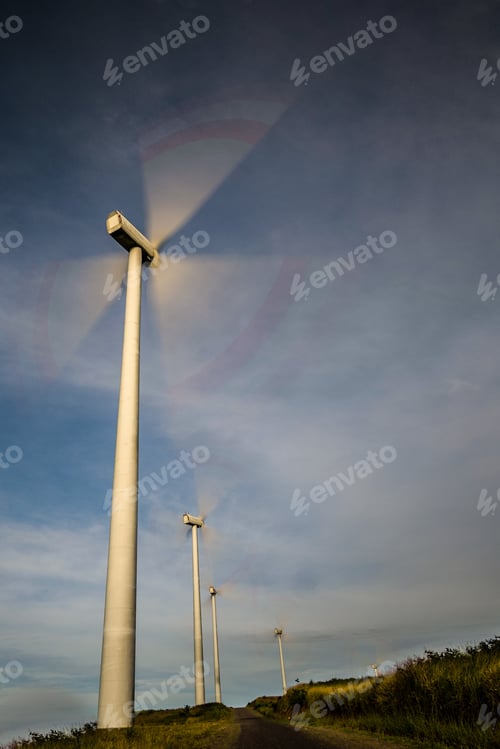 Preview: Vertical shot of windmills on the road covered in the grass under the sunlight at daytime