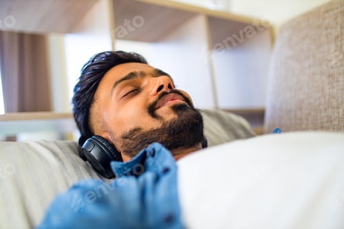 Preview: asian indian man living room lying on sofa closing his eyes and listening to music