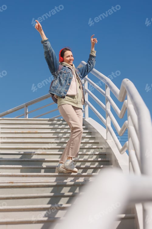 Preview: woman dances and sings on stairs, listens to music or podcast with red headphones, full-length