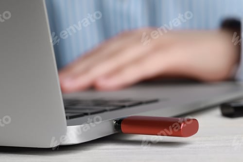 Preview: Woman using laptop with attached usb flash drive at wooden table, closeup