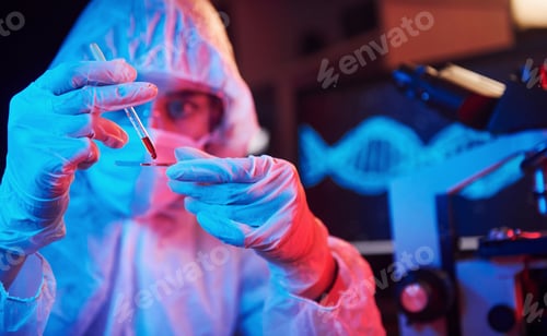 Preview: Nurse in mask and white uniform, holding tube with liquid and sitting in neon lighted laboratory
