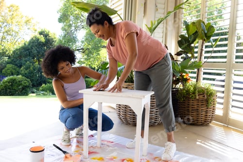 Preview: Biracial mother and adult daughter painting furniture outside at home in an upcycling project