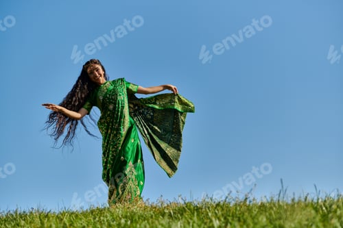 Preview: summer dance of cheerful indian woman in traditional attire in green field under blue sky