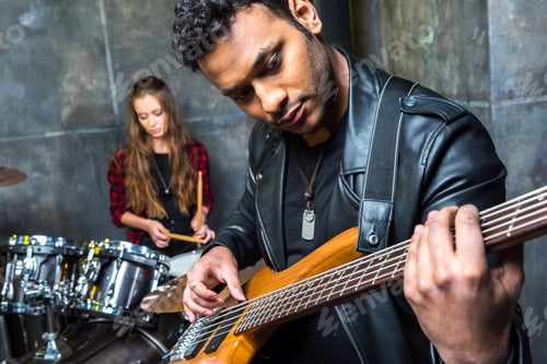 Preview: portrait of man playing guitar with woman playing drums behind, electric guitar player concept