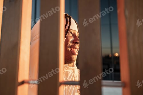 Preview: happy african american man smiling at sunset over the city. - view through a fence -