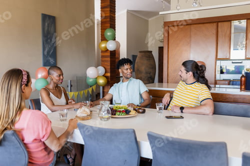 Preview: Friends enjoying conversation and sharing food at dining table in modern home